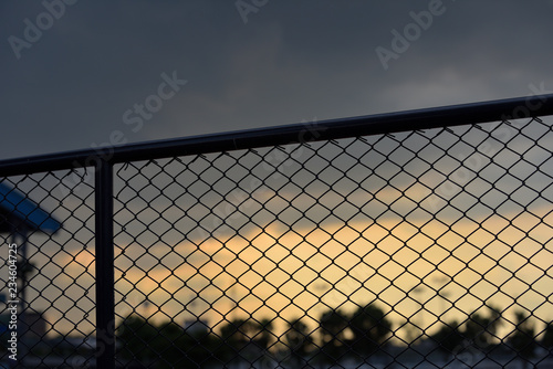 A close-up of a silhouette chain link fence in a sport field with a nice scene of a sun set as a background. 