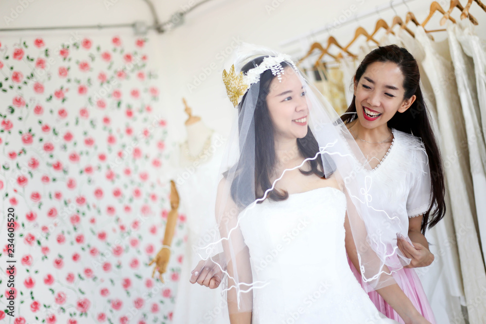 Beautiful bride getting dressed by her best friend in her wedding day and choosing a wedding dress in the shop and the shop assistant is helping her Beautiful bride getting dressed by her best friend in her wedding day and choosing a wedding dress in the shop and the shop assistant is helping her