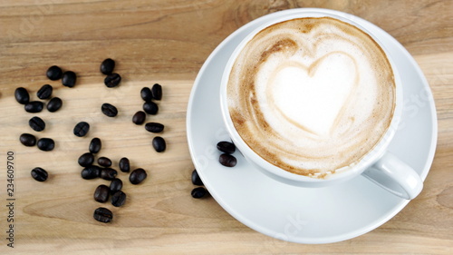 Cappuccino or latte art coffee. Free hand pouring some hearts of milk on top. A white ceramic cup on the wood table with some coffee beans. The best food and drink in the world. Fresh energy everyday.