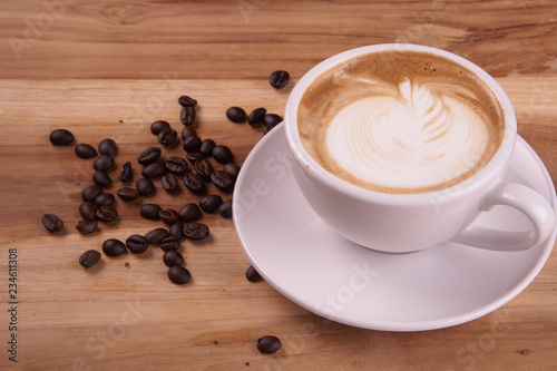 Cappuccino or latte art coffee. Free hand pouring some foam of milk on top. A white ceramic cup on the wood table with some coffee beans. The best food and drink in the world. Fresh energy everyday.