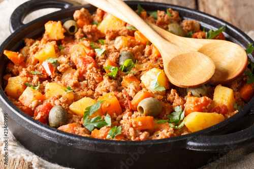 picadillo is a traditional dish made with ground beef, potatoes, onions, garlic, cumin, carrots, white wine, tomato sauce, raisins, olives and capers closeup. horizontal photo