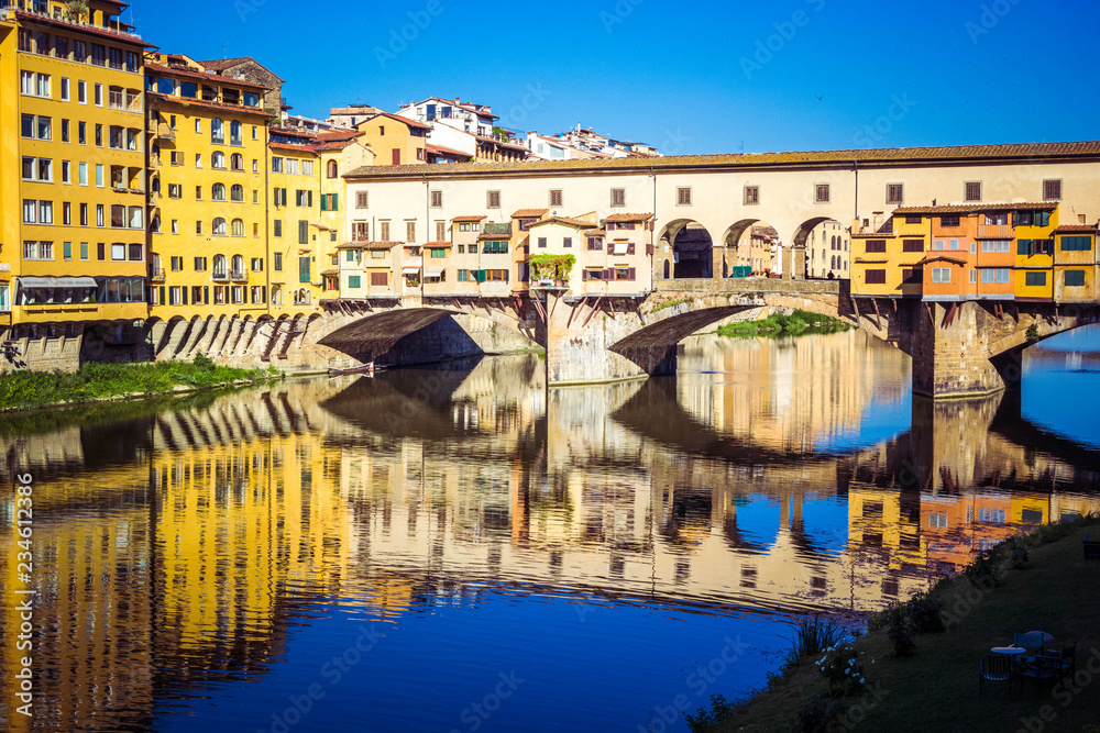 Panoramic view of the Arno River and stone medieval bridge Ponte Vecchio with beautiful reflection of colorful houses, Florence, Tuscany, Italy.