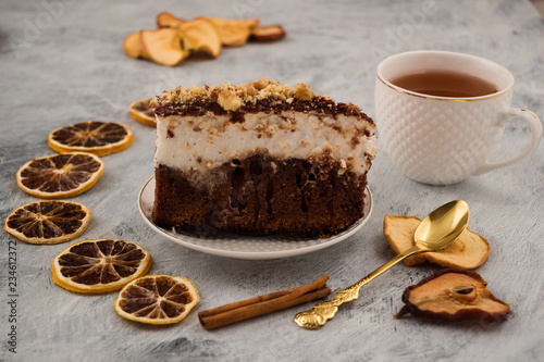 A sliced piece of cake with a white meringue. Grated nuts, chocolate batter. A portion of the festive dessert. Dried slices of lemon, pear, Apple. Cinnamon stick. Tea in white mug. Light background.
