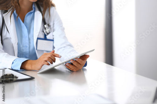 Unknown doctor woman using tablet computer while standing straight near window in hospital, close-up of hands. Medicine and health care concept photo
