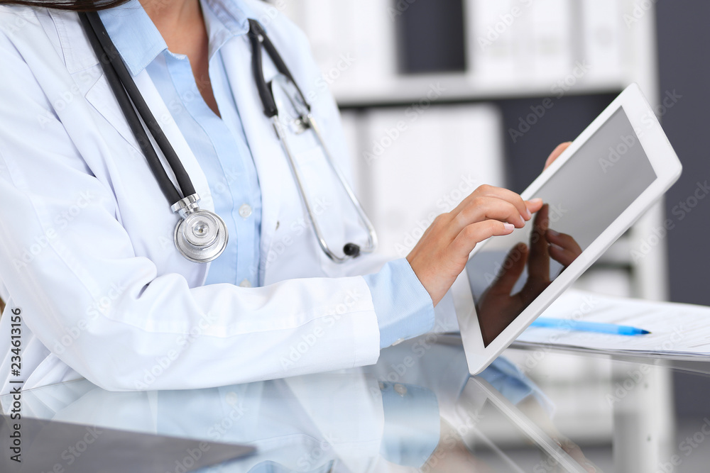Close-up of female physician hands using digital tablet while sitting at glass desk at hospital office. Medicine and healthcare concept Close-up of female physician hands using digital tablet while sitting at glass desk at hospital office. Medicine and healthcare concept