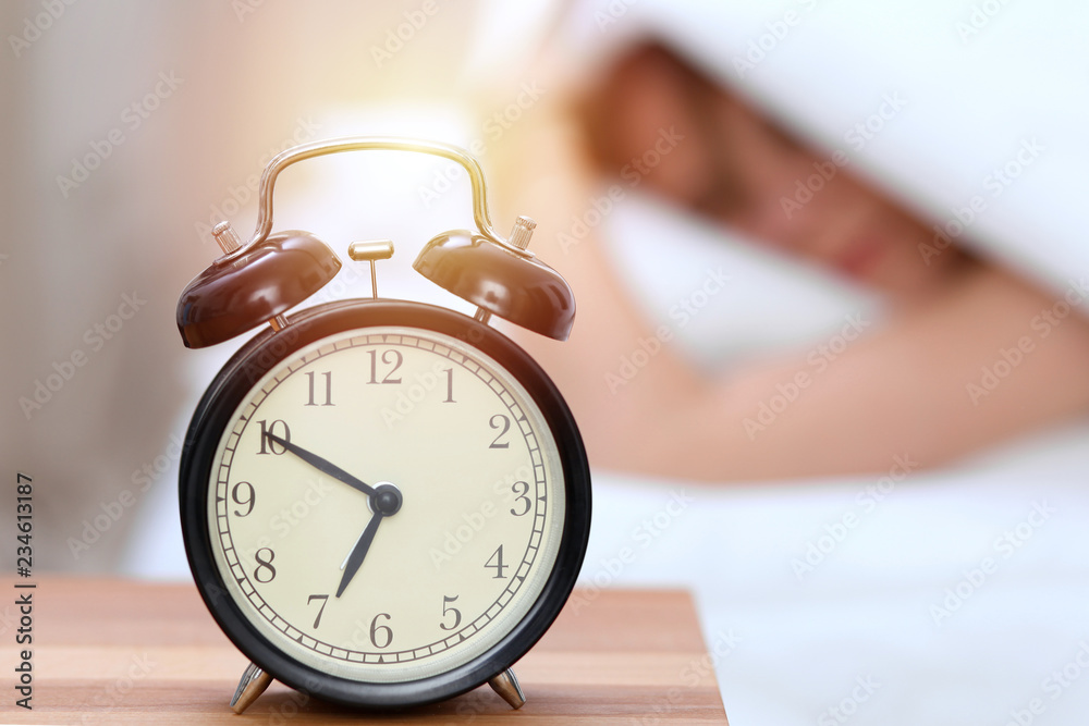 Alarm clock opposite of sleepy young woman. Early wake up, not getting enough sleep concept Alarm clock opposite of sleepy young woman. Early wake up, not getting enough sleep concept