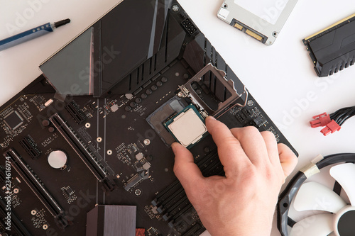 Top view of man hands puts cpu on motherboard, computer parts, Electronics repair and upgrade on white desk background, copy space. Motherboard, processor cpu, cooler, radiator, flat lay.