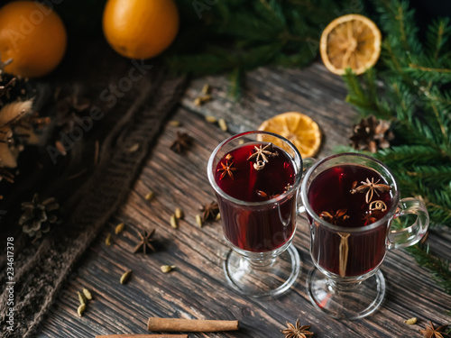 two glasses of mulled wine with spices and orange slices on a wooden table. Hot alcoholic drink on the background of Christmas decor with fir branches and cones