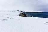 coast with blue cold water of the Arctic Ocean with stones under a layer of white snow in the frosty winter
