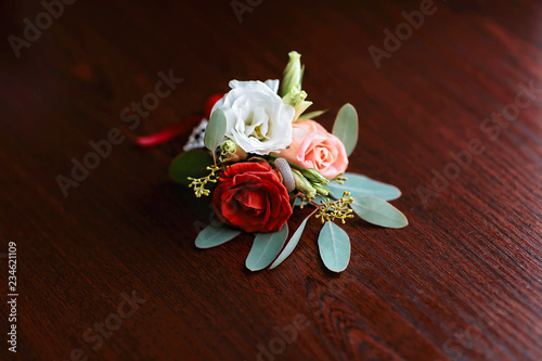 wedding accessories of the budo of red, white and pink flowers for the groom with a ring on a dark wooden background photo