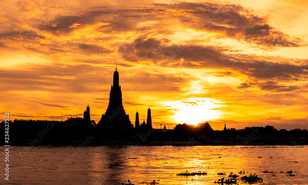 River and Wat Arun Ratchawararam at sunset with beautiful  orange sky and clouds. Wat Arun buddhist temple is the landmark in Bangkok, Thailand. Silhouette dramatic sky and temple in Thailand.