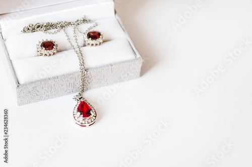 Jewelry set with red gems in the box close-up. Silver necklace and earrings with ruby gem. Gift, present. Celebration theme. Festive background with copy space. Selective focus