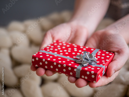 Red gift box with gray bow in the children's hands on wool background