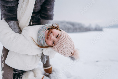 Mother and her little daughter are playing together near the winter forest. They are jumping and having fun. Winter and Christmas mood