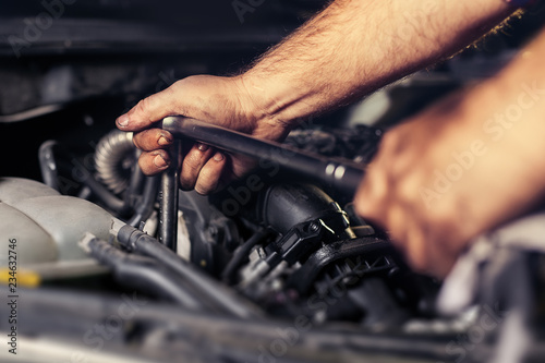 Hands repairing a car engine with a wrench