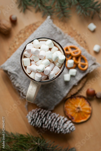 A cup of hot latte with marshmallows and some salty pretzels on wooden table. Christmas time, winter season.