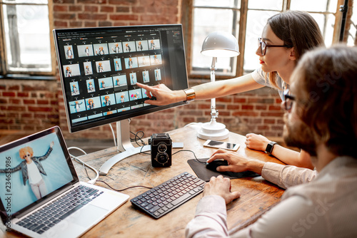 Young couple of photographers working with woman's portraits at the working place with two computers in the studio