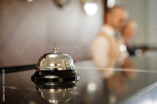 Modern luxury Hotel Reception Counter desk with Bell.  Service Bell locating at reception. Silver Call Bell on table, Receptionists on background. heck in hotel. Concept. photo