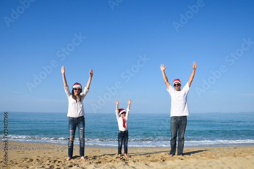 Happy family in Christmas Hats having fun on sandy beach. New Year holidays concept