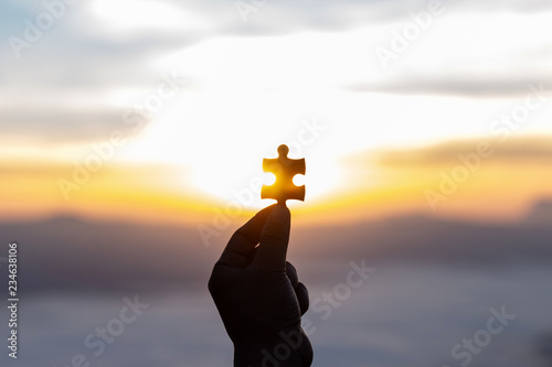 hands holding piece of red jigsaw puzzle and morning sunrise background
