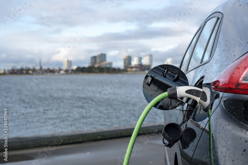 Charging an electric car, with the city and water in the background, green charging cable and black car. copenhagen