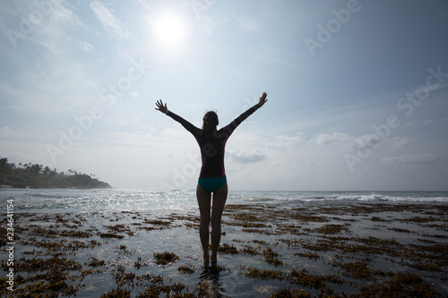 Happy Freedom Woman outstretched arms reaching the sky at Sunrise on the seaside reef