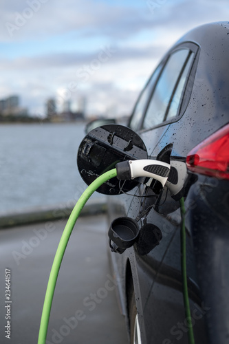 Charging an electric car, with the city and water in the background, green charging cable and black car. copenhagen