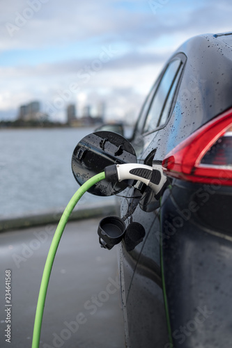 Charging an electric car, with the city and water in the background, green charging cable and black car. copenhagen