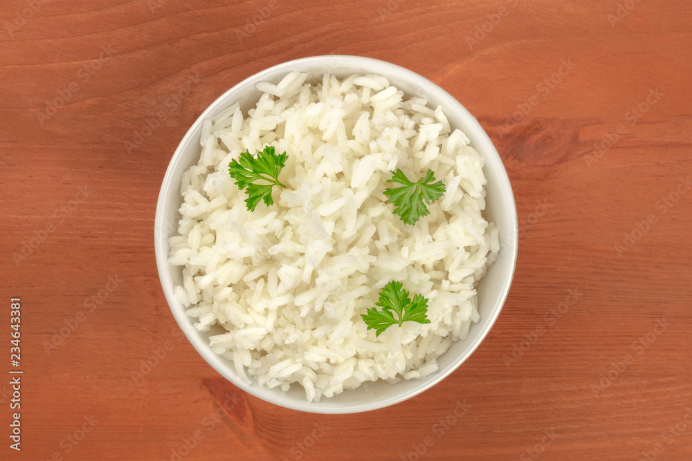 A bowl of cooked white jasmine rice, garnished with parsley leaves, shot from the top on a rustic wooden background with a place for text A bowl of cooked white jasmine rice, garnished with parsley leaves, shot from the top on a rustic wooden background with a place for text