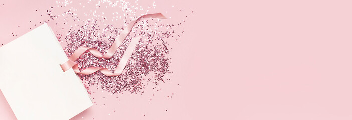 Flat lay top view White gift bag and holographic glitter confetti in the form of stars on pink background. Greeting card Festive holiday pastel backdrop. Birthday congratulations Christmas New Year