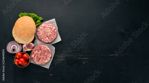 Preparation of burger. Meat, fresh vegetables, tomatoes, onions. On a black wooden background. Top view. Free copy space.