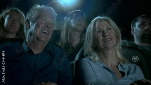Older couple at the movie theatre laughing at a comedy film.