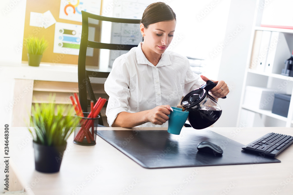 A young girl sitting at a table in the office and pours coffee into a Cup. A young girl sitting at a table in the office and pours coffee into a Cup.