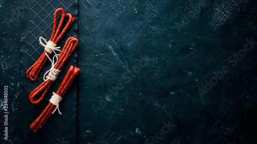 Sausages Kabanosi. On a black stone background. Top view. Free copy space. photo