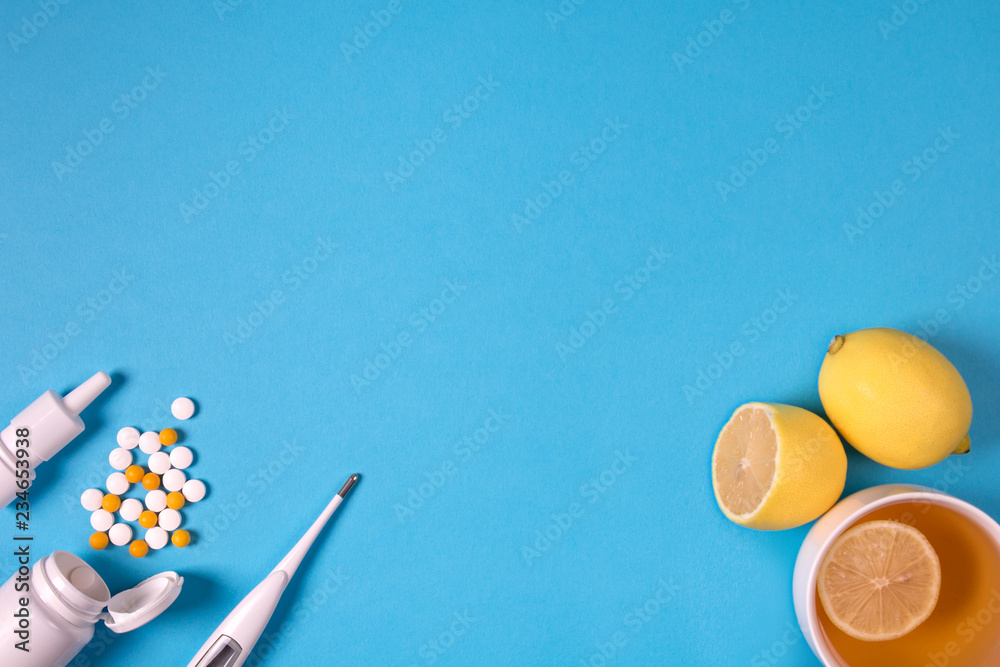 Medical electronic thermometer, medication bottle with pills, spray for nose and tea with lemon on blue background. Health care concept. Herbal and chemical medicine. Top view. Copy space. Flat lay