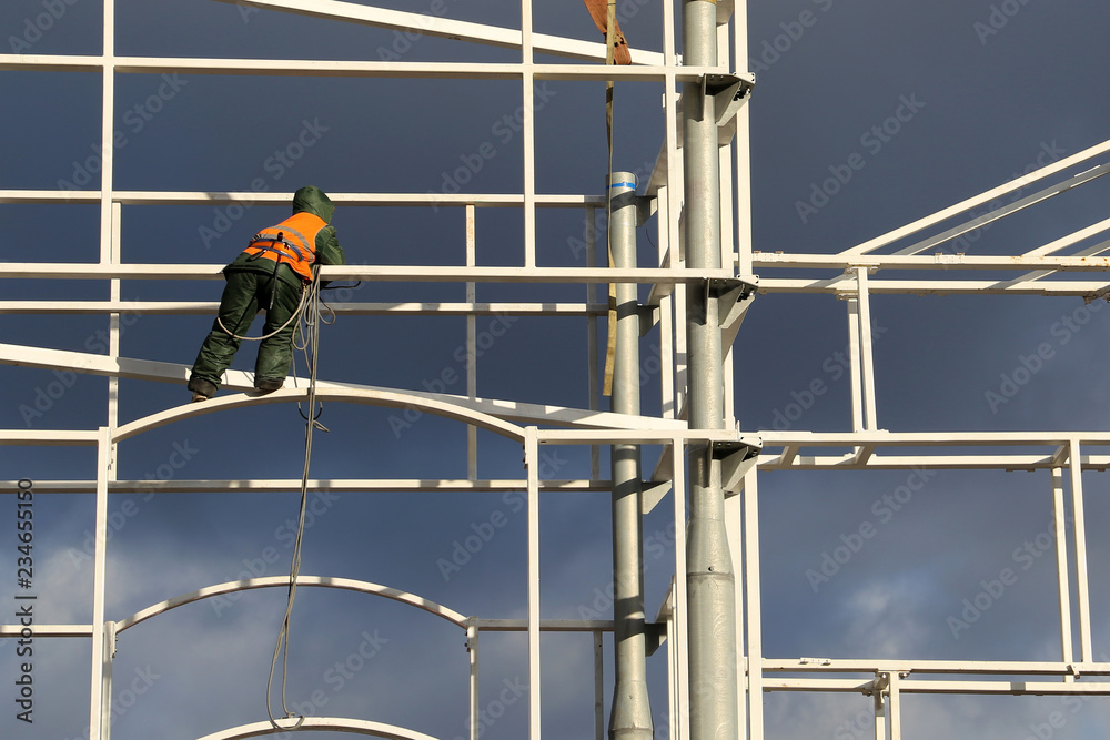 Construction worker working on scaffolding. High-altitude installer on the construction site on stormy sky background