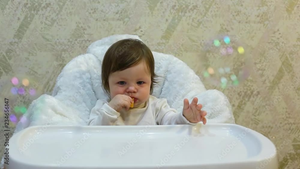 Cute toddler girl eats tangerine slice with appetite and catches soap bubbles Cute toddler girl eats tangerine slice with appetite and catches soap bubbles