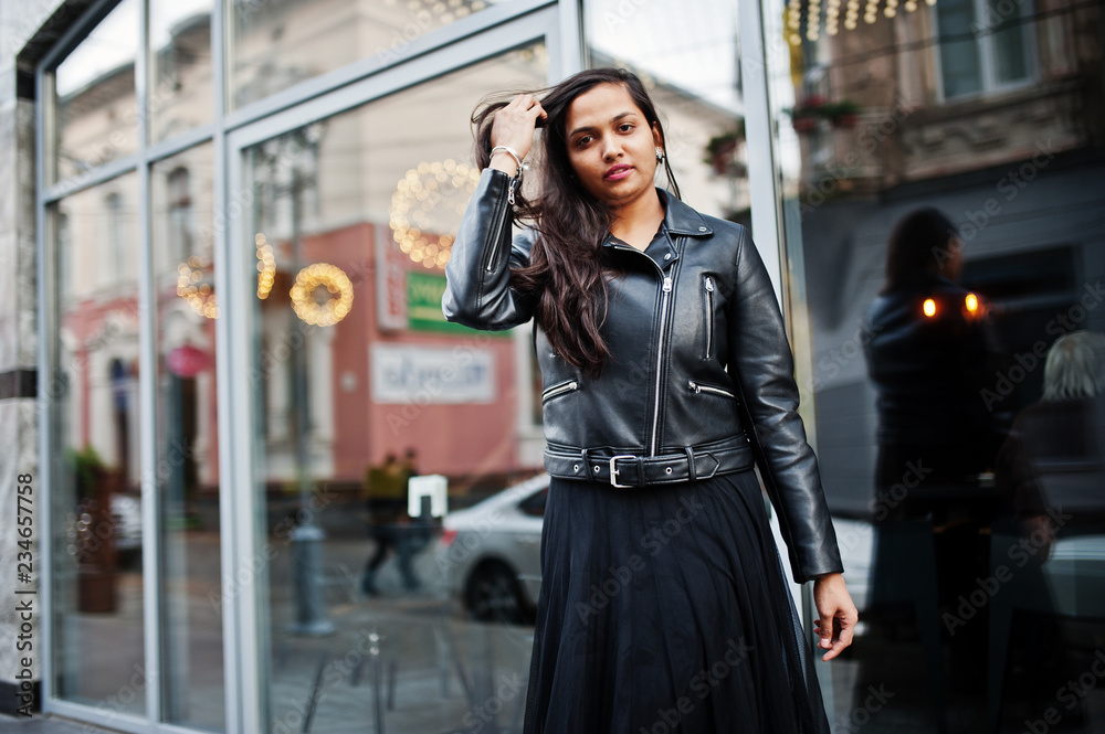 Pretty indian girl in black saree dress and leather jacket posed outdoor at street.