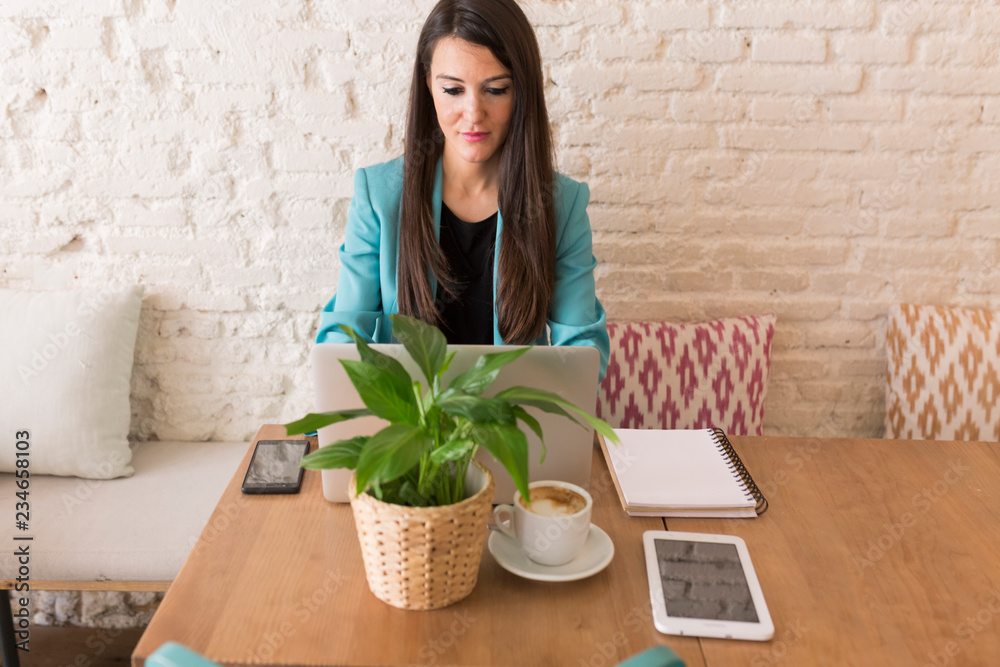portrait of a young beautiful woman using mobile phone in a restaurant. She is smiling. Modern life of a blogger with computer laptop, tablet, notebook and coffee on table. Casual clothes. Lifestyle portrait of a young beautiful woman using mobile phone in a restaurant. She is smiling. Modern life of a blogger with computer laptop, tablet, notebook and coffee on table. Casual clothes. Lifestyle