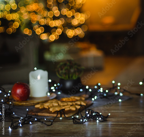 Christmas background - decorated with lights and garlands Christmas tree in the house. In the foreground is a table with ginger biscuits and a garland. Blurred focus.