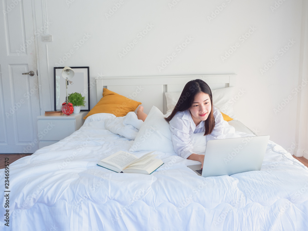 asian woman using computer and read book on bed in the morning asian woman using computer and read book on bed in the morning
