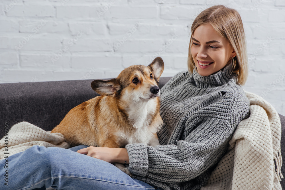 smiling young woman lying on sofa with adorable pembroke welsh corgi dog