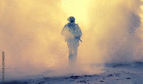 Special operations forces soldier, army ranger or commando in camo uniform, helmet and ballistic glasses walking at battlefield covered with smoke. Airsoft war game player coming through smoke screen photo