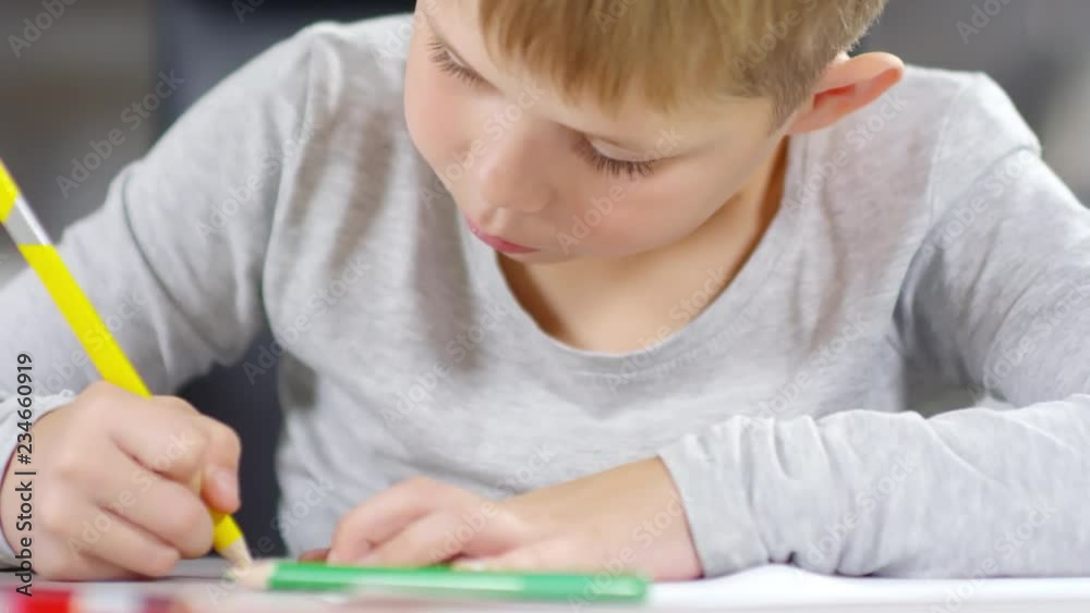 Close-up view of little Caucasian boy drawing with colored pencils at table Close-up view of little Caucasian boy drawing with colored pencils at table