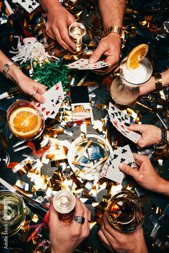 cropped image of friends with alcoholic cocktails playing poker at table covered by golden confetti