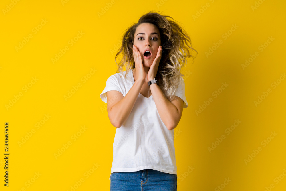 Beautiful young blonde woman jumping happy and surprised over isolated yellow background Beautiful young blonde woman jumping happy and surprised over isolated yellow background