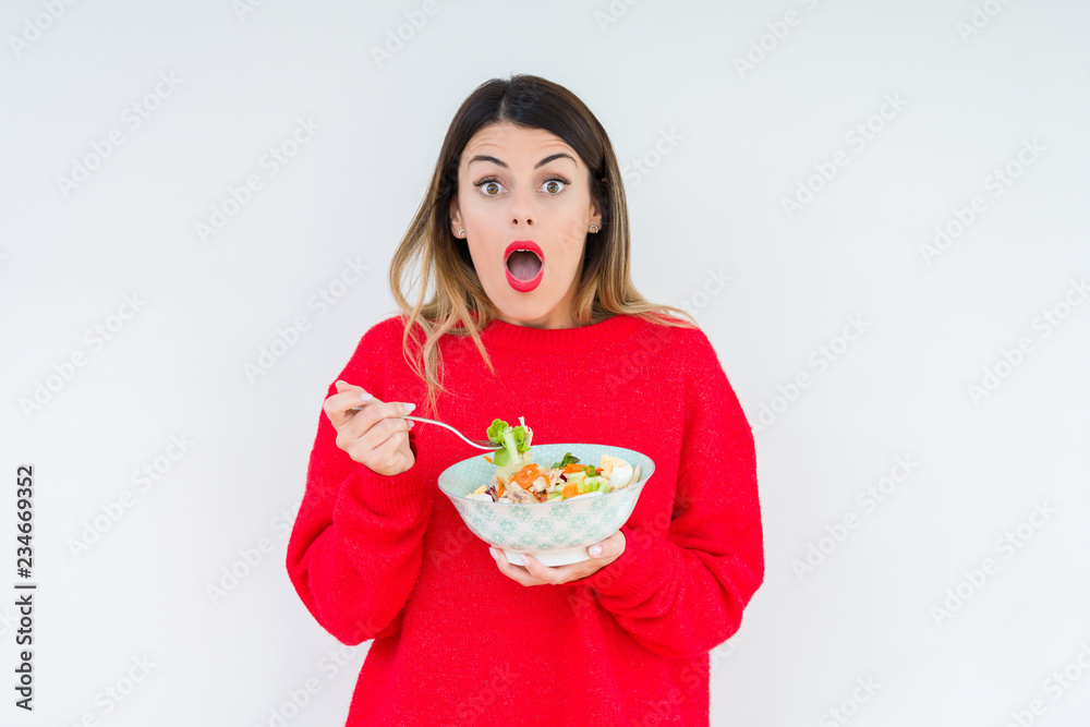 Young woman eating fresh healthy salad over isolated background scared in shock with a surprise face, afraid and excited with fear expression Young woman eating fresh healthy salad over isolated background scared in shock with a surprise face, afraid and excited with fear expression