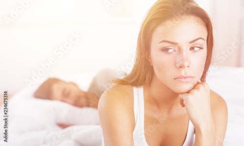 Dissatisfied beautiful young woman in bed with sad expression on