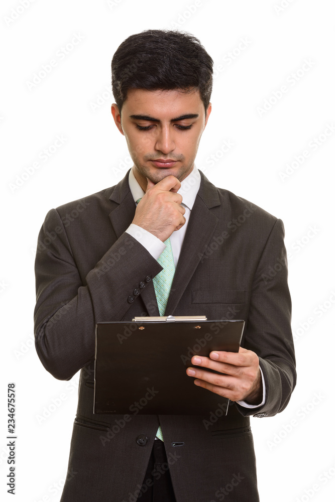 Young handsome Persian businessman reading clipboard while think Young handsome Persian businessman reading clipboard while think