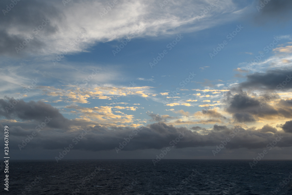 Dark sunset sky over the ocean. Illuminated by the setting sun clouds on the background of blue gaps. Dark sunset sky over the ocean. Illuminated by the setting sun clouds on the background of blue gaps.
